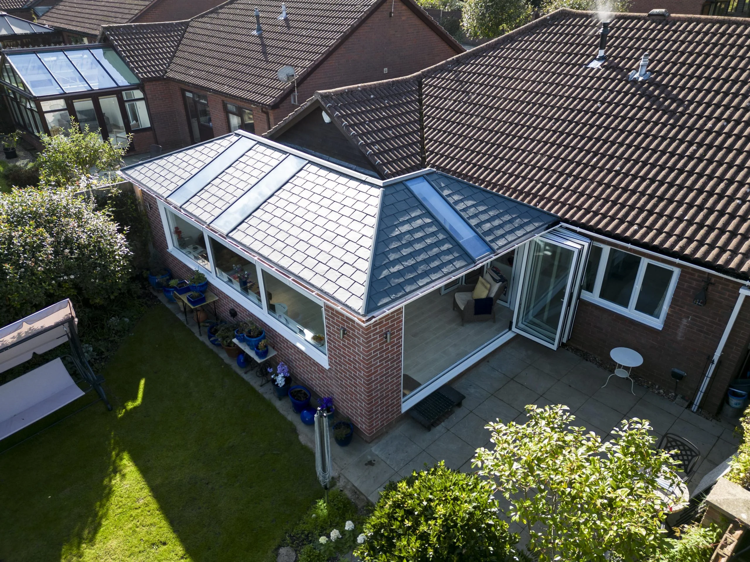 UK conservatory extension in bungalow with white bi-fold doors open leading to large back garden
