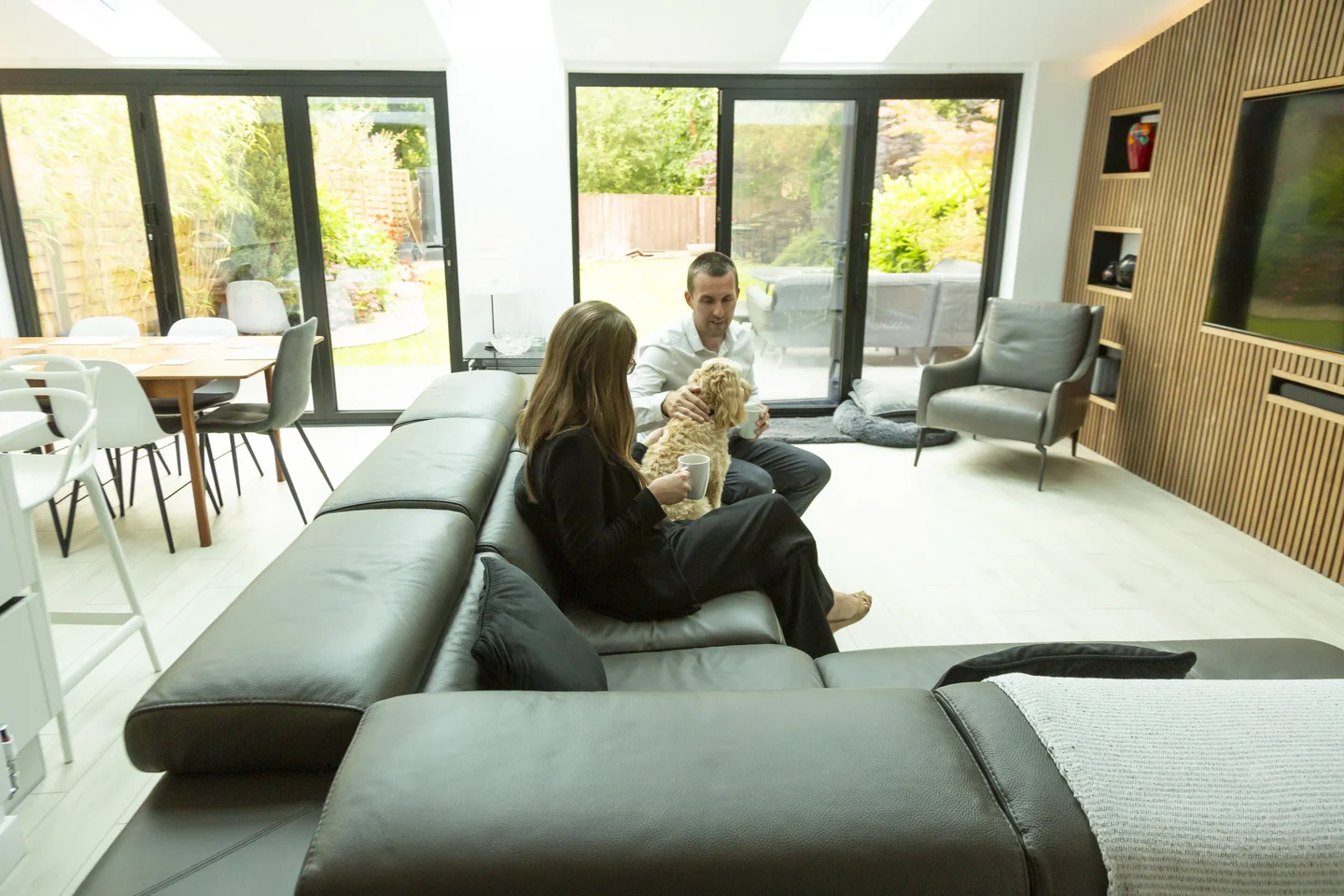 Couple sitting down with dog on sofa in open plan lounge
