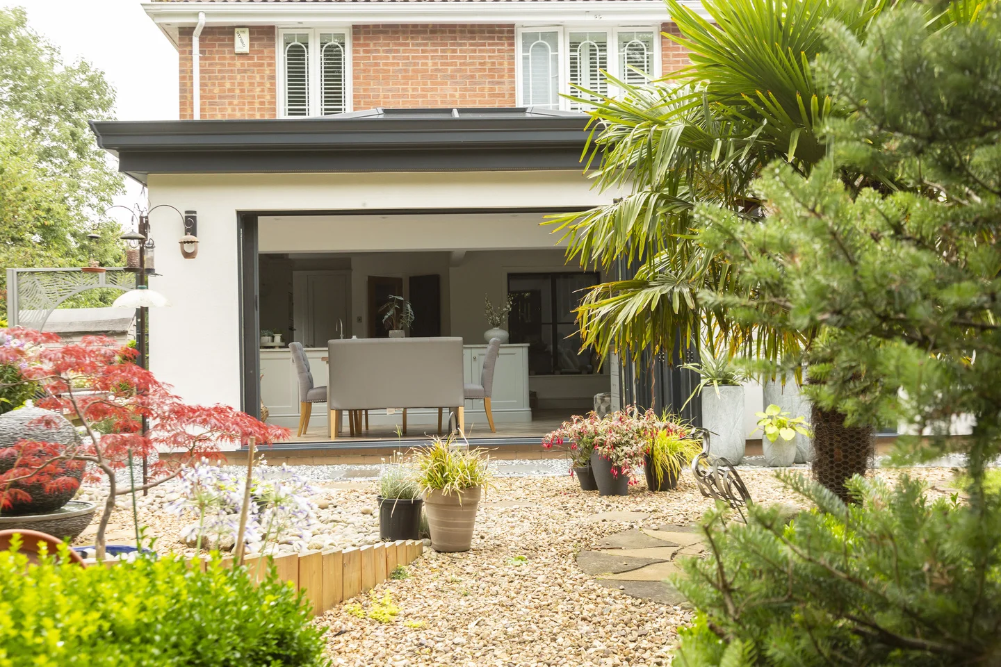 Green garden with large outdoor plants and trees with view of house extension