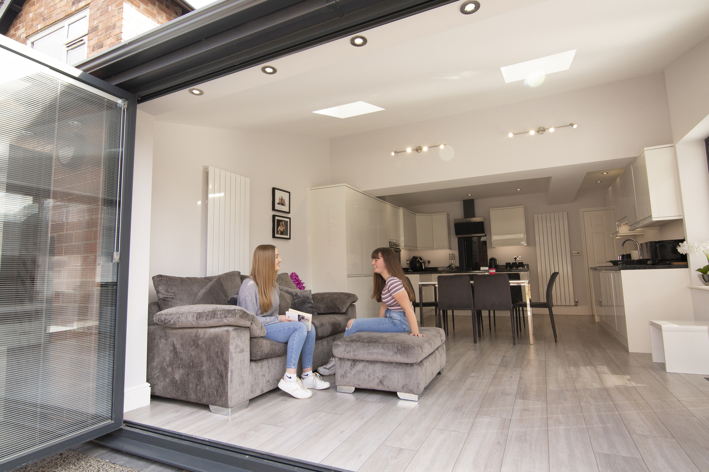 Two sisters and family dog sitting on comfy grey sofa with bi-fold doors open