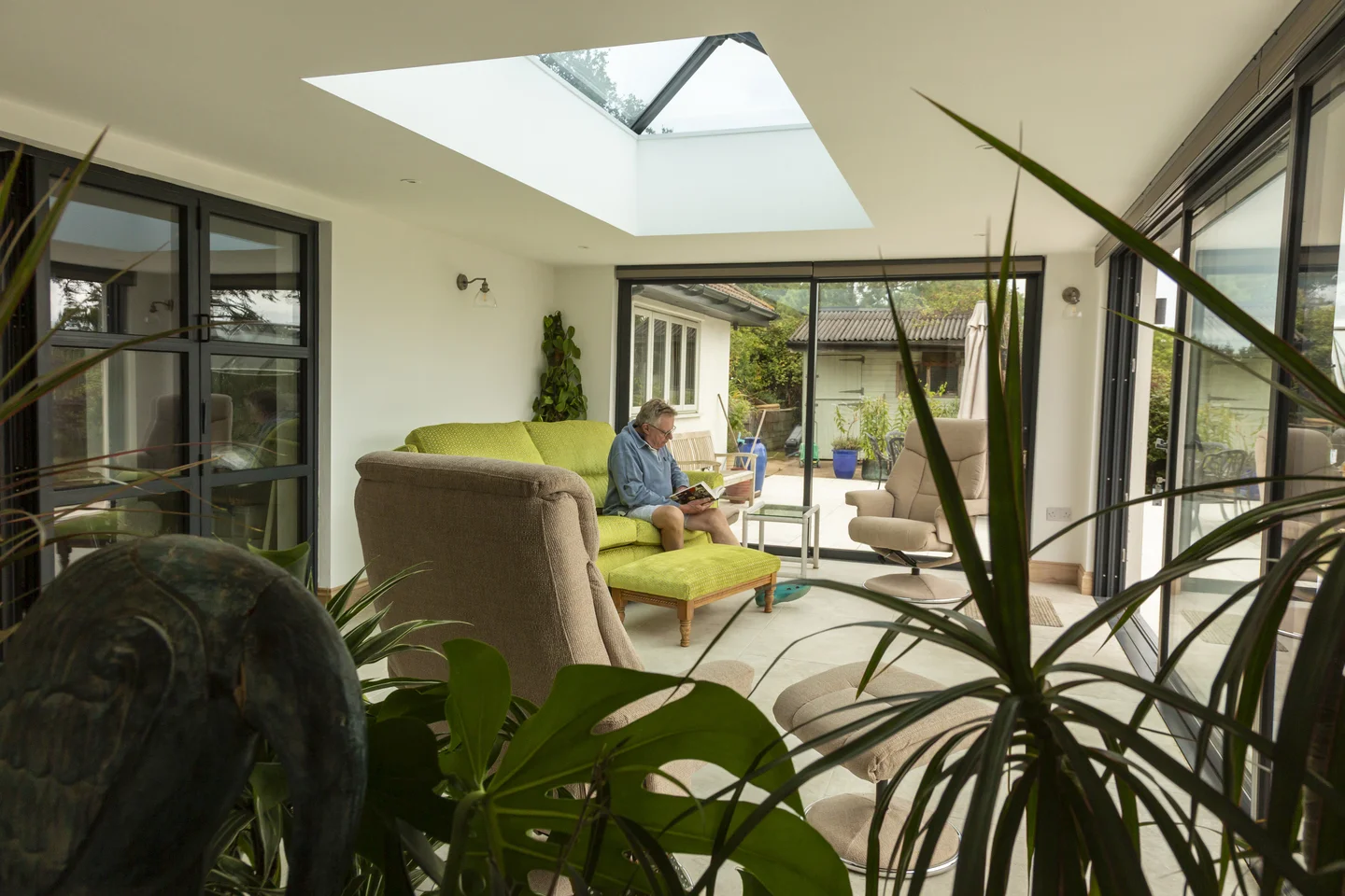 Elderly man sitting down reading on bright green sofa in large extension room