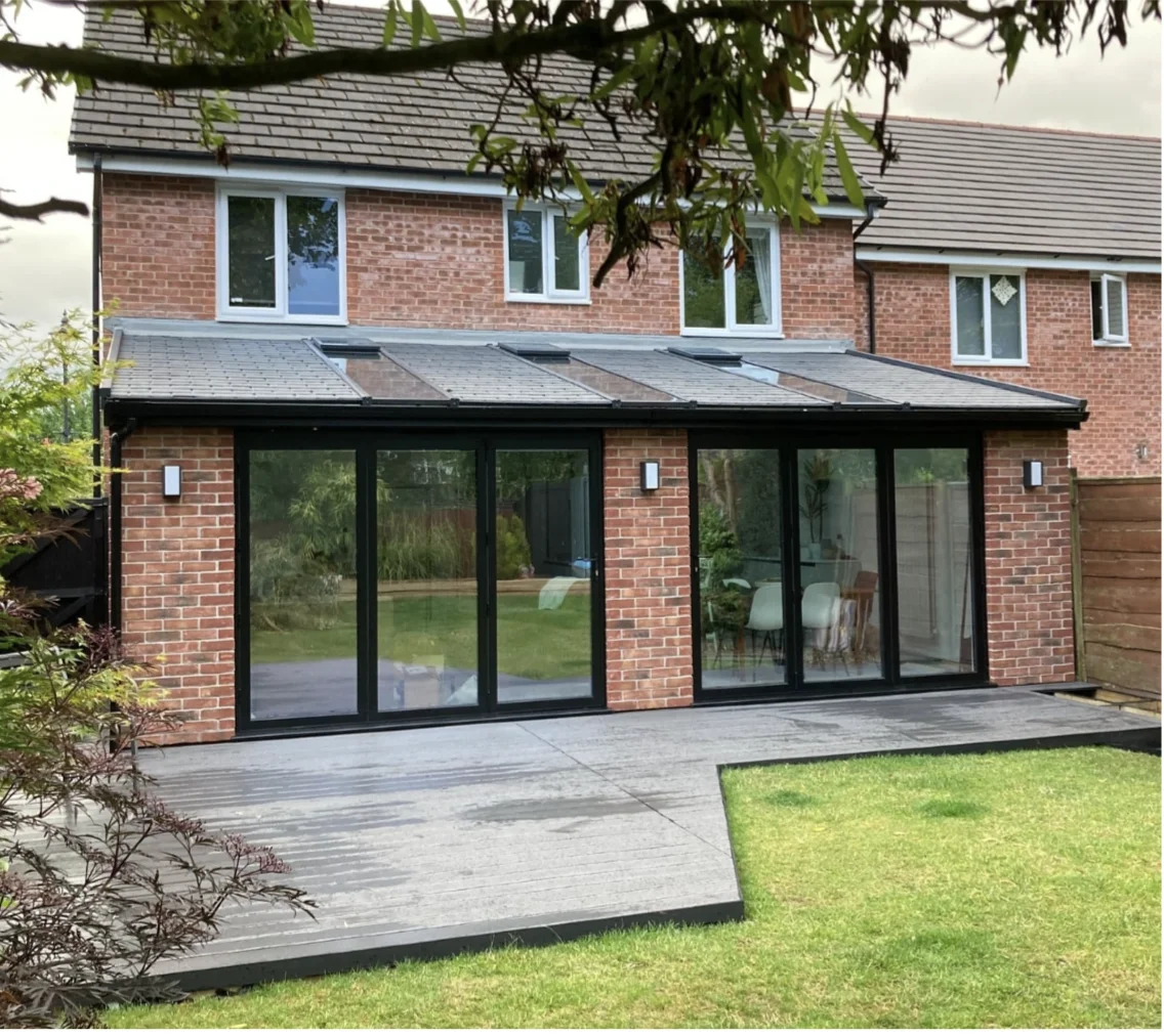 Brick home extension with black framed glass doors and grey garden patio